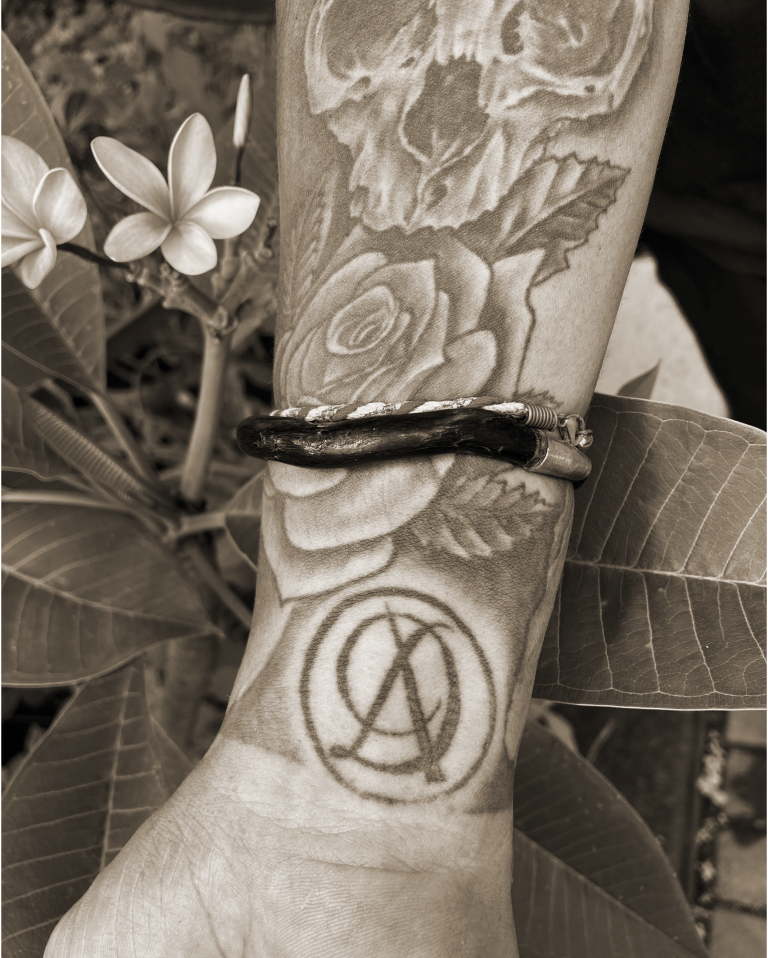 A monochromatic edited photo of a hand with a tattooed Divka Antik logo - the logo is derived as a monogram of a combination of the letters D and A in a circle.