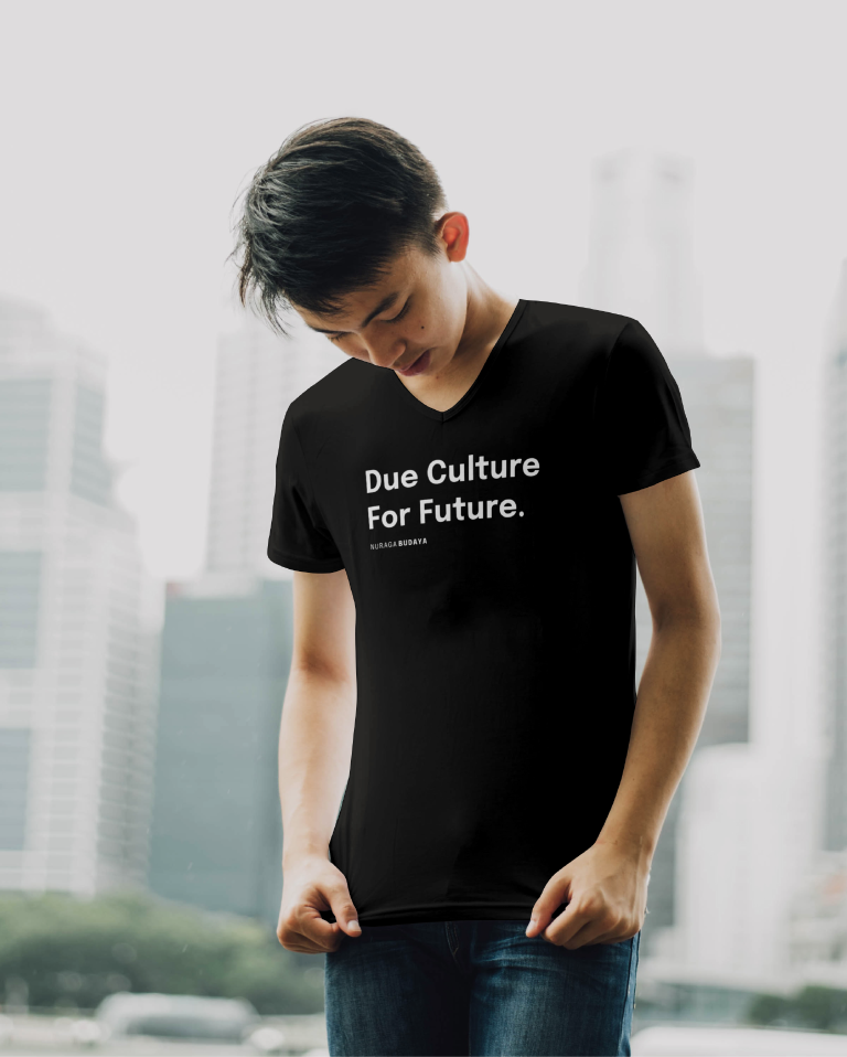 Photo of a young Asian man wearing a black t-shirt with a claim Due Culture Fot Future in white placed across his chest, with a horizontal version of the Nuraga Budaya logo below. There are blurred skyscrapers in the background of the photo.